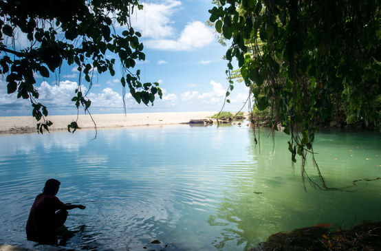 Seorang perempuan duduk di sebuah teluk yang berbatuan dan berpantai pasir.