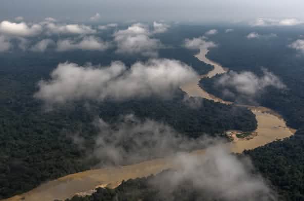 Foto dari udara: Sungai berkelok-kelok merayap di hutan hujan yang ditutupi awan