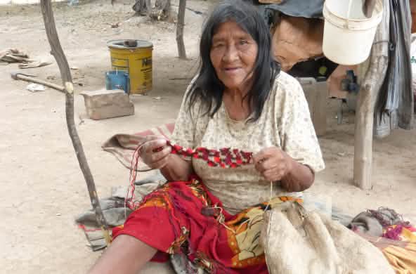 Seorang perempuan masyarakat adat yang duduk di atas tanah membuat rajutan dari serat tumbuhan.