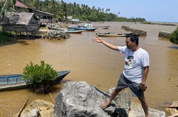 Muhammad al amien dari Aliansi Sulawesi menunjuk dengan tangannya perairan yang telah tercemar di tepi pantai tropis