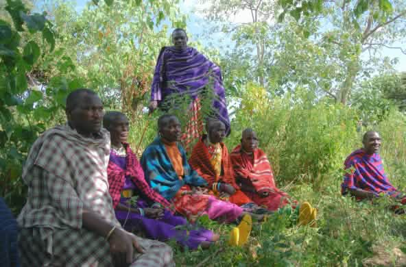 Sekelompok pria suku Maasai duduk di atas rumput dengan pakaian tradisional berwarna-warni