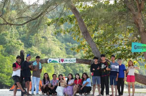 Sebuah kelompok anak muda sedang duduk dan berdiri di depan pohon di pantai
