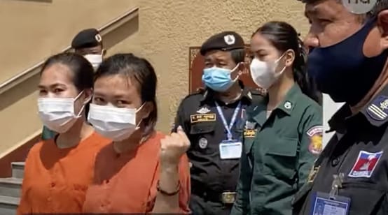 Dua tahanan perempuan dengan pakaian berkabung berwarna oranye, di belakangnya polisi