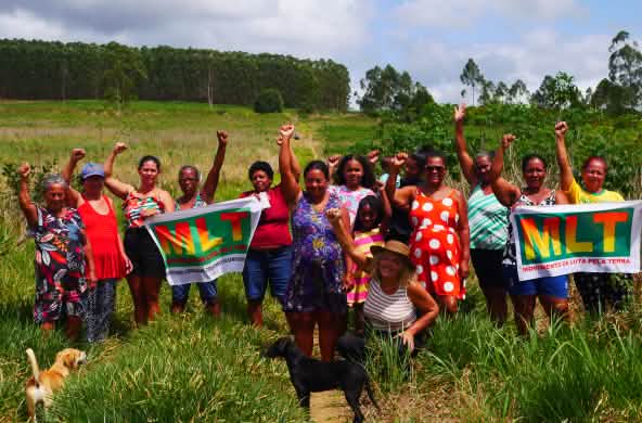Sebuah kelompok dari 15 perempuan dalam aksi protes dengan kepalan tangan diangkat tinggi dan dua spanduk yang bertuliskan MLT