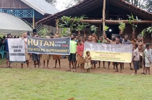 Demo masyarakat adat Yei dengan spanduk di depan sebuah rumah