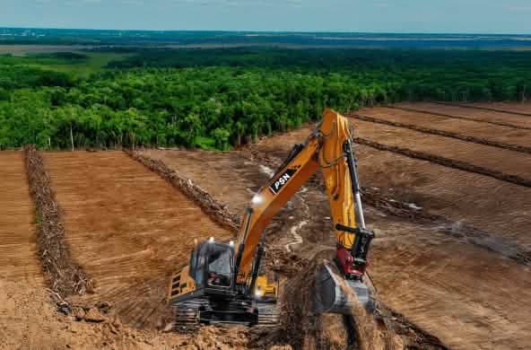 ekskavator dengan tulisan PSN diatas lahan gundul, di belakang ada hutan hujan yang terancam