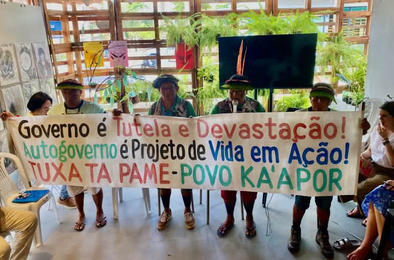 Empat anggota masyarakat adat Ka´apor di ruangan rapat mengangkat sebuah spanduk yang penuh dengan tulisan