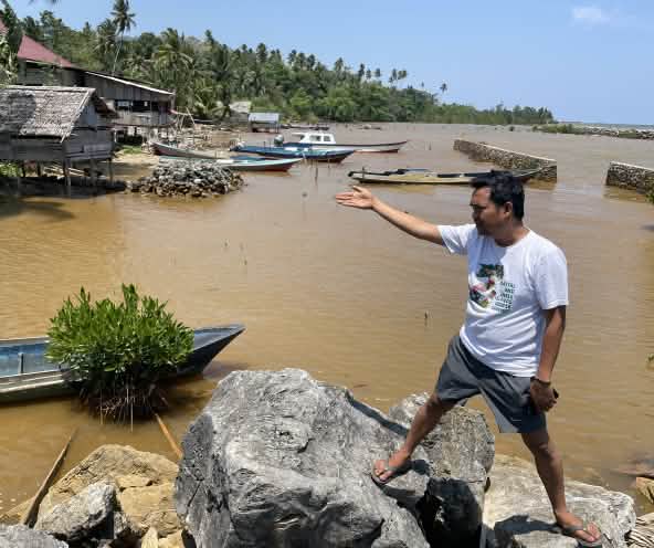 Muhammad al Amien dari Aliansi Sulawesi menunjuk dengan tangannya perairan yang telah tercemar di tepi pantai tropis