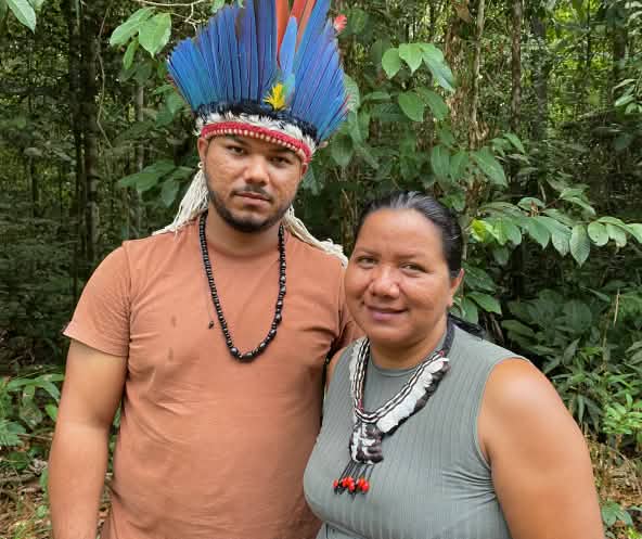 Foto seorang perempuan masyarakat adat dengan kalung berbulu dan seorang pria masyarakat adat dengan mahkota berbulu