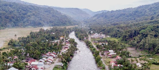Sungai mengalir melalui kampung, di belakang ada pergunungan