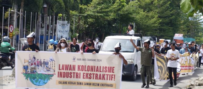 Demo – tampak depan: spanduk “Lawan Kolonialisme Industri Ekstraktif”, tampak belakang: peserta demo dan sebuah mobil pick-up