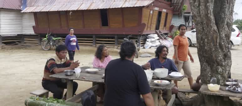 4 orang duduk di depan meja di luar rumah dengan latar belakang rumah tradisi Batak