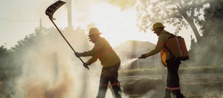 Dua laki-laki dengan alat tepuk padam api dan ransel air dengan selang semprot di tengah-tengah asap dari kebakaran hutan