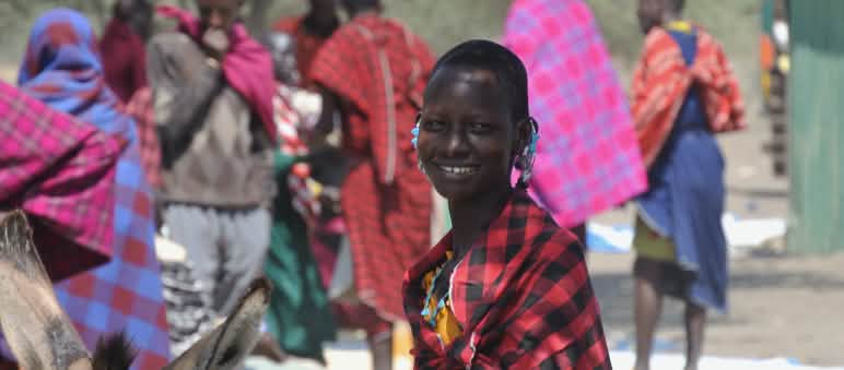 Suku Maasai di sebuah pasar dekat kawah Ngorongoro Perempuan dan laki-laki suku Maasai dengan sarung berwarna-warni di pasar, seorang perempuan menatap kamera