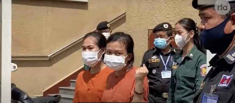 Dua tahanan perempuan dengan pakaian berkabung berwarna oranye, di belakangnya polisi