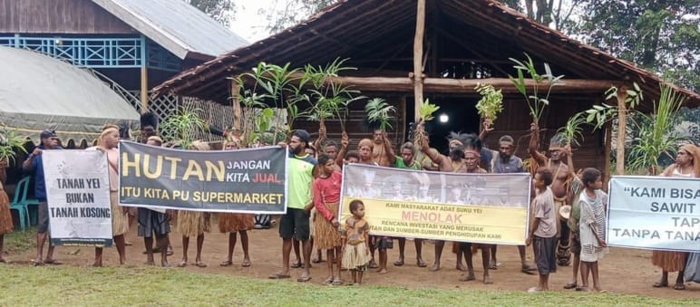 Demo masyarakat adat Yei dengan spanduk di depan sebuah rumah