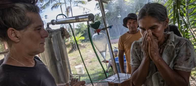 Seorang perempuan masyarakat adat yang berada di samping alat distilasi uap mencium bau minyak eteris yang diteteskan ke tangannya oleh seorang pengajar