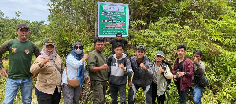 beberapa orang didepan tanda yang melarag semua kegiatan di hutan produksi