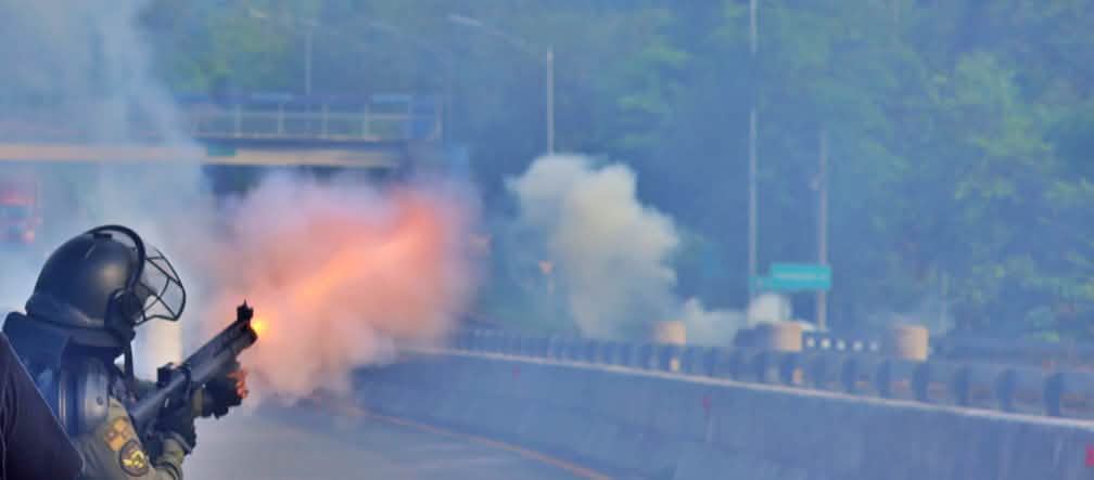 Seorang polisi dengan pakaian pelindung melepaskan tembakan gas air mata di sebuah jalan tol yang kosong.