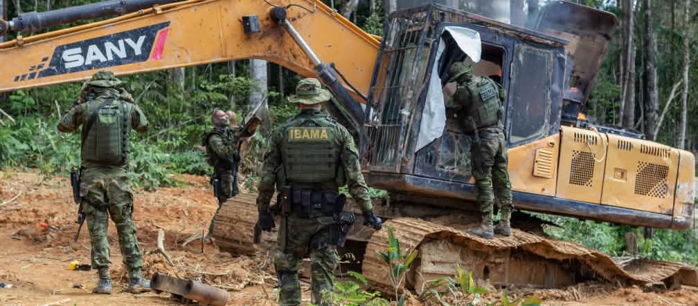 Polisi bersenjata dari Dinas Lingkungan Hidup (IBAMA) merusak sebuah eksavator yang digunakan oleh pertambangan emas ilegal di hutan hujan masyarakat adat Munduruku Sekelompok petugas dari Dinas Lingkungan Hidup (IBAMA) dengan seragam menyamar merusak sebuah eksavator berwarna kuning di hutan hujan
