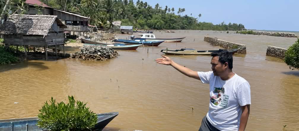 Muhammad al amien dari Aliansi Sulawesi menunjuk dengan tangannya perairan yang telah tercemar di tepi pantai tropis