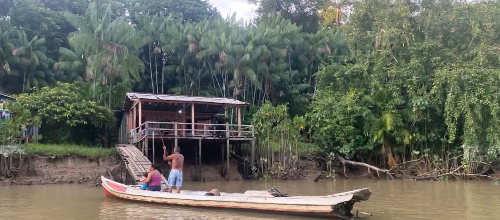 Dua warga desa di dalam perahu kayu di depan gubuk kayu di tepi sungai di hutan hujan