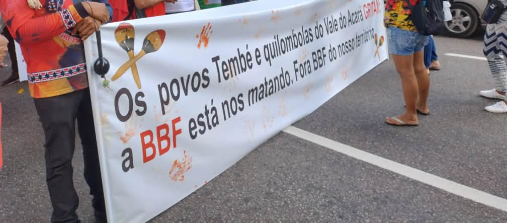 Aksi protes kelompok masyarakat adat dengan spanduk besar di sebuah jalan di sebuah kota: Tulisan di spanduk: Warga Temnbé dan Quilombola dari lembah Acará: BBF membunuh kami. BBF keluar dari wilayah kami