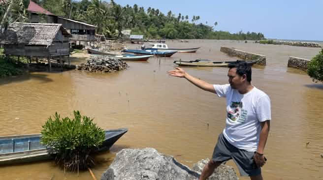 Muhammad al amien dari Aliansi Sulawesi menunjuk dengan tangannya perairan yang telah tercemar di tepi pantai tropis