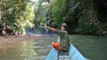 Seorang pria di tepi perahu kecil dengan antusiasnya menunjuk hutan hujan