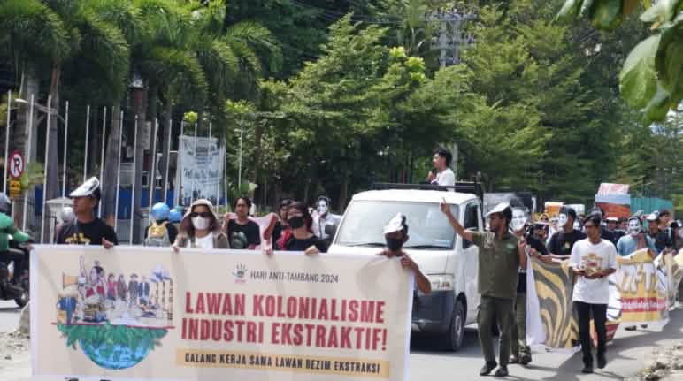Dengan berbagai aksi, teater, musik dan pameran, para penjaga lingkungan dan warga yang terkena dampak menentang perusakan oleh pertambangan Demo – tampak depan: spanduk “Lawan Kolonialisme Industri Ekstraktif”, tampak belakang: peserta demo dan sebuah mobil pick-up