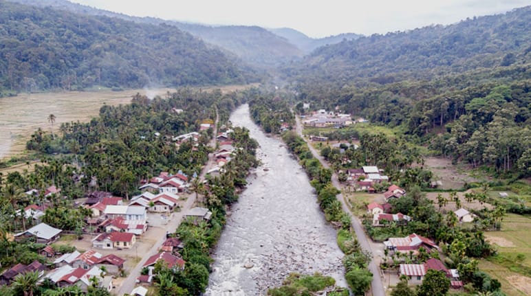 Sungai mengalir melalui kampung, di belakang ada pergunungan