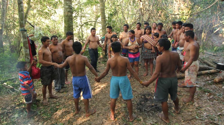 Masyarakat adat Ka'apor  – anak-anak, perempuan dan laki-laki saling berpegangan tangan dan berdiri berlingkar di hutan hujan