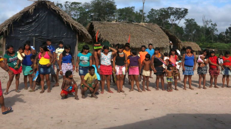 Masyarakat adat Kaapor berdiri membentuk dua barisan di depan gubuk di hutan hujan