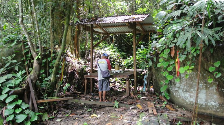 Sembahyang di depan altar di hutan, disampingnya terdapat tebing bebatuan dan dibawahnya aliran air kecil Altar di hutan hujan