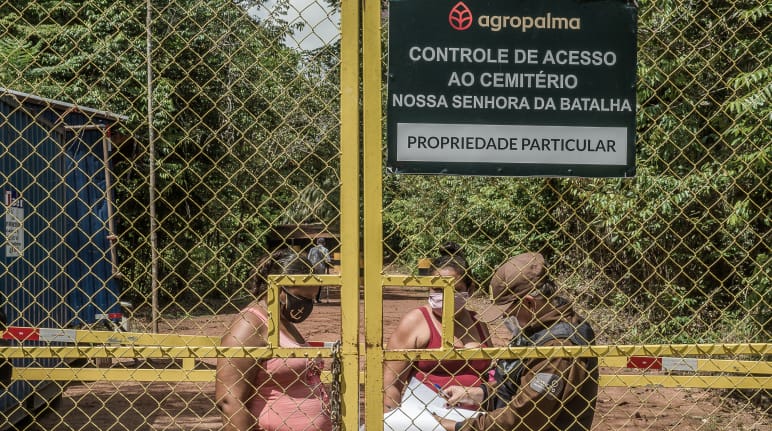 Dua perempuan dibelakang gerbang tinggi diperiksa pihak keamanan. Tulisan di papan perusahaan: Agropalma. Pemeriksaan jalan masuk menuju pemakaman Nossa Senhora da Batalha. Milik pribadi