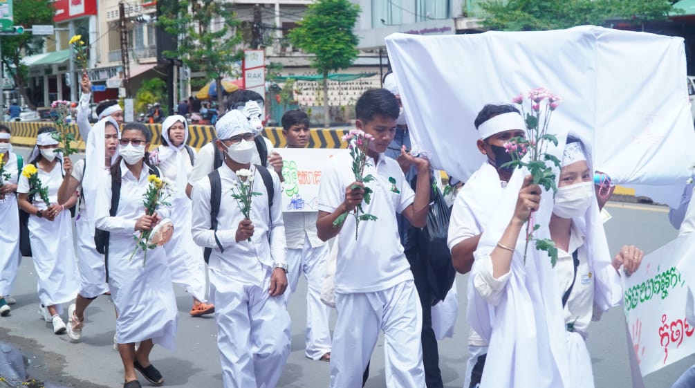 Sekelompok anak muda berpakaian putih berjalan dengan bunga di tangan melewati jalan di Phnom Penh
