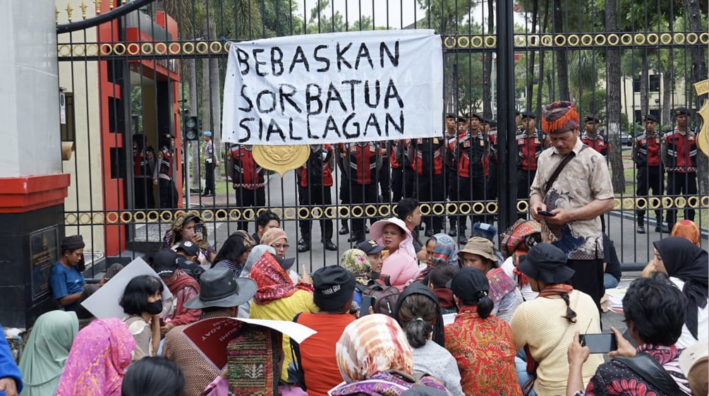 Demonstrasi di depan pagar tinggi dengan spanduk „Bebaskan Sorbatua Siallagan“