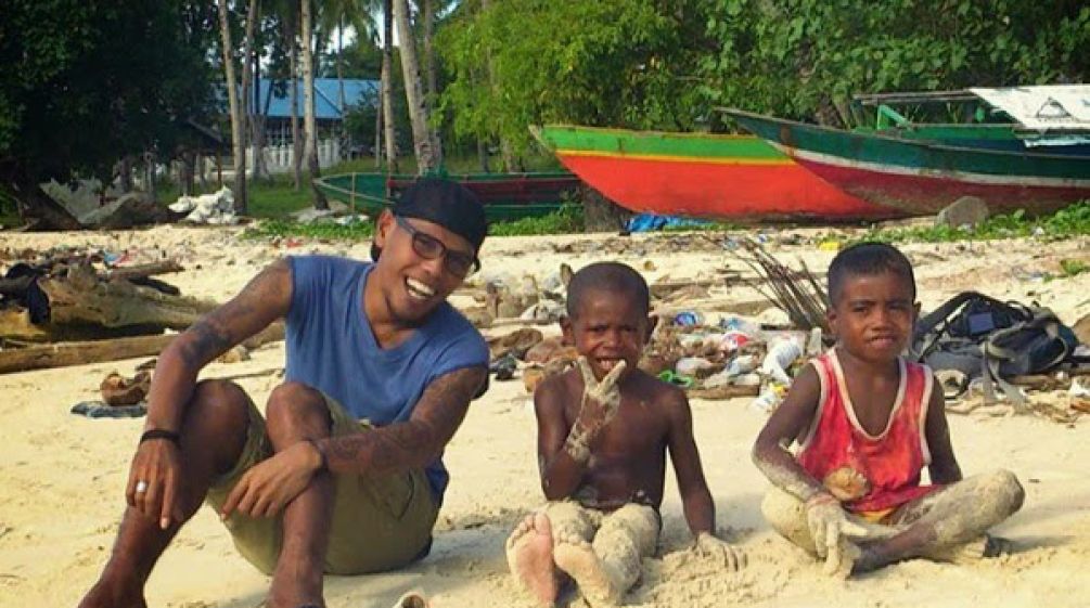 Jopi Peranginangin sedang duduk dengan dua remaja di pantai dan tertawa ke arah kamera.